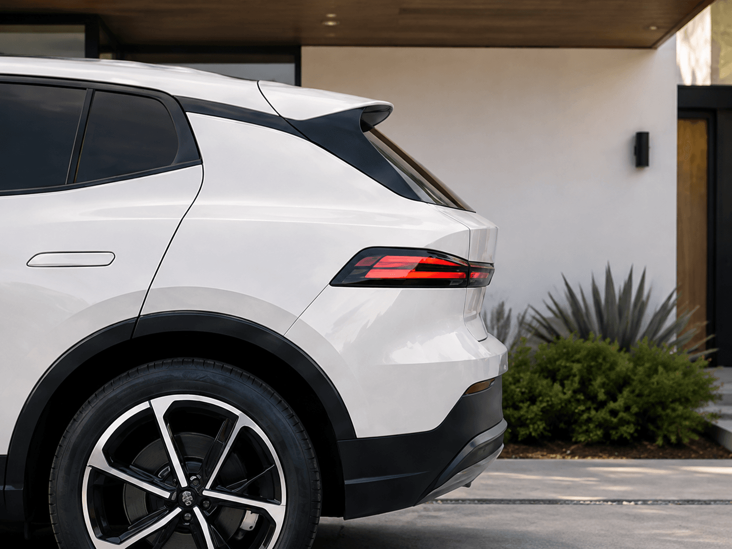 Rear side of a white electric vehicle parked beside a home